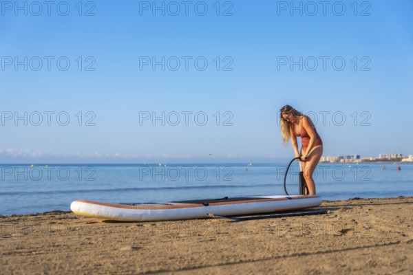 Woman inflating a paddleboard on a sandy beach, ready for a summer day of paddle surfing under a