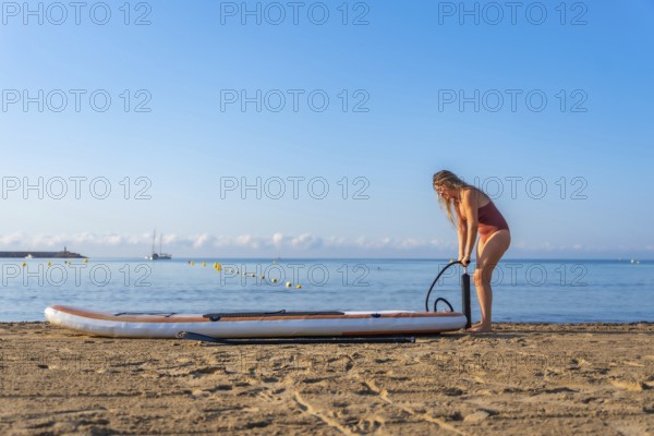 Woman inflating her paddle board on a beautiful sandy beach, preparing for a summer adventure on