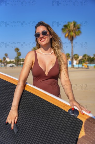 Smiling woman carrying her paddle board along a sunny beach, embracing the excitement of a summer