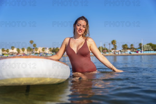 Young woman enjoying paddle surfing in the calm sea on a sunny summer day, embracing the