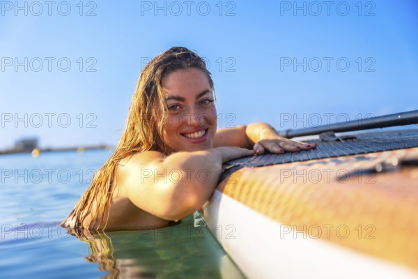 Cheerful woman relaxing on a paddleboard in clear blue water, embracing the joy of summer and