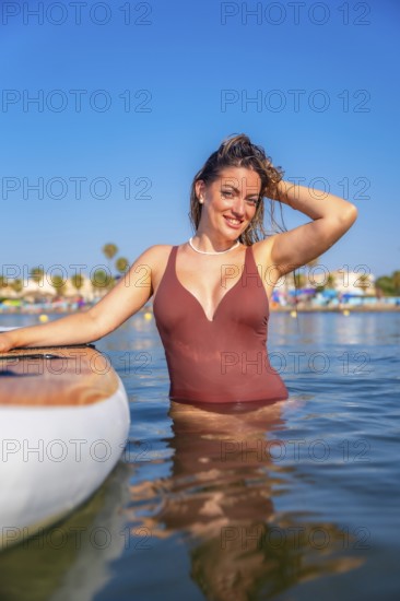 Young woman enjoying summer vacation, posing in the sea next to her paddle board, wearing a