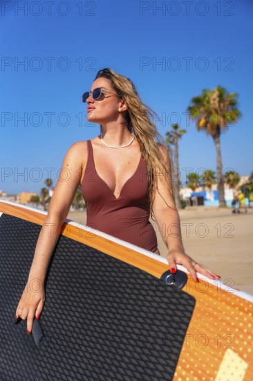 Surfer holding her paddle board on a sunny summer day at the beach, soaking up the sun and feeling