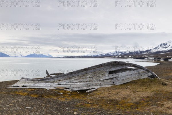 Broken wooden boat on the beach, mountain range, snow, sea, arctic spring, Bamsebu, Spitsbergen,