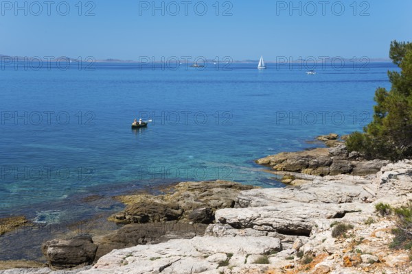 Rocky coast with clear water and sailing boat under blue sky, Slanica, town of Murter, island of