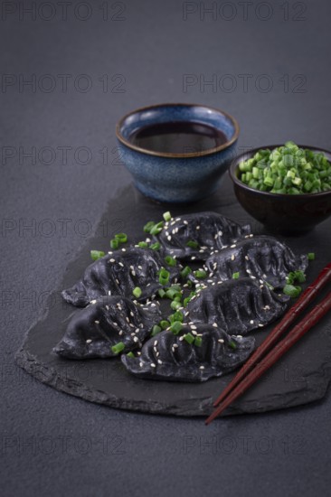 Japanese gyoza dumplings, made of black dough, black gyoza, with green onions and sauce, on a