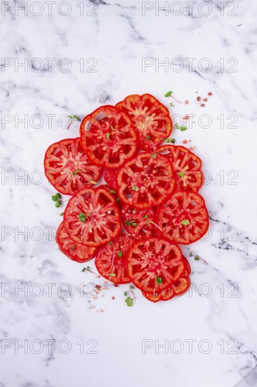 Freshly sliced ripe tomatoes arranged on a marble surface with microgreens and sea salt for a