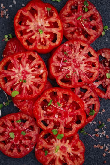 Freshly sliced ripe tomatoes arranged on a textured dark surface with herbs and salt scattered