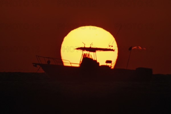 The sun rises behind a boat on the Costa Rei, a coastal stretch of the Italian Mediterranean island