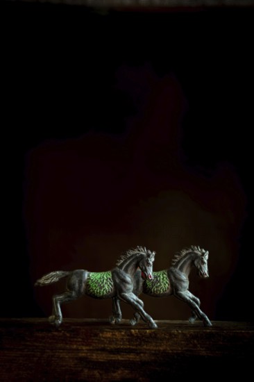 Two intricately designed horse figurines are positioned side by side, appearing to run forward. The