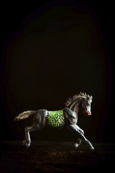 A black horse figurine is captured in mid-gallop, showcasing detailed green patterns on its side.