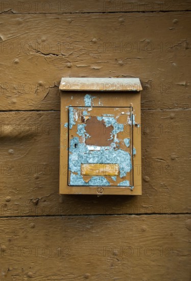 A weathered mailbox hangs on a rustic wooden wall, showcasing chipped paint in blue and brown tones