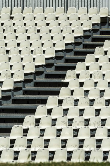 Empty white seats neatly arranged in rows await spectators at a stadium. The absence of an audience