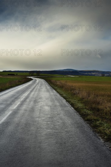 A winding road stretches through green fields under a cloudy sky, showcasing the beauty of the