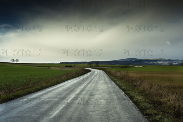 A winding road stretches through green fields under a cloudy sky, showcasing the beauty of the