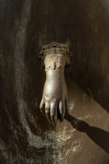 A decorative hand-shaped door knocker is firmly mounted on a weathered wooden door showcasing rich