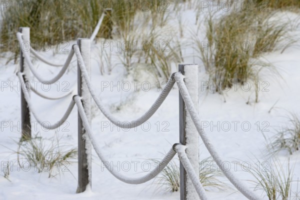 Winter day, onset of winter, demarcation poles with ropes in the snow-covered dune landscape of
