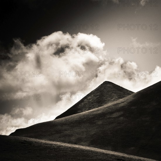A striking view of a mountain peak stands tall against a backdrop of swirling clouds. Sancy Massif,
