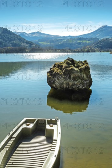 Lake chambon reflects the stunning blue sky and surrounding mountains. A small boat rests at the