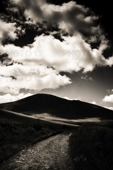 A winding path leads towards a dark mountain silhouette against a dramatic sky filled with