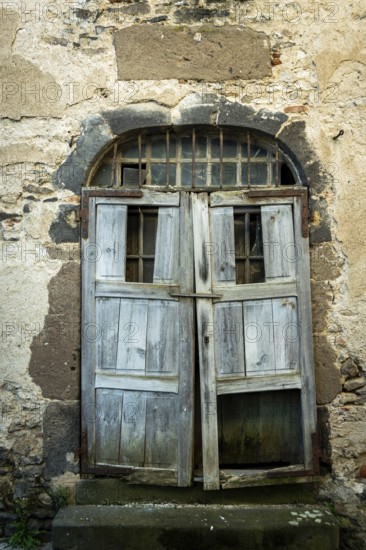 A rustic wooden door stands ajar in an aged stone wall, showing signs of weathering and decay. The