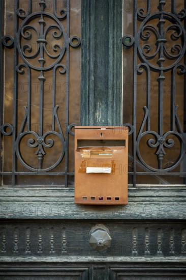 A rusty mailbox is affixed to a beautifully crafted wrought iron door. The intricate ironwork