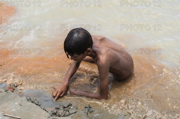 A boy sits in the bank of Brahmaputra River as he bathe to seek relief from the intense summer heat