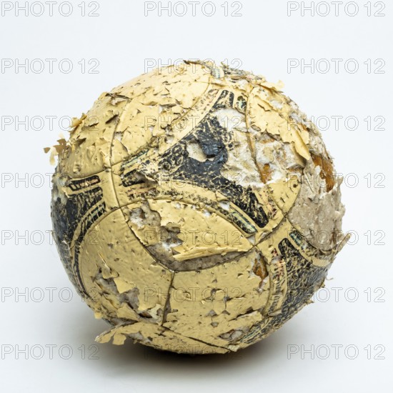 A worn football ball rests against a neutral background, displaying significant peeling and faded