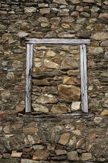 This rustic wall features a stone layout with various textures, framed by an aged wooden window.