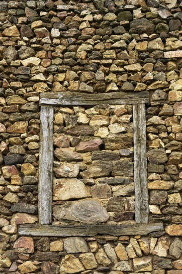 A wall constructed of unevenly arranged stones features a striking wooden frame that outlines an