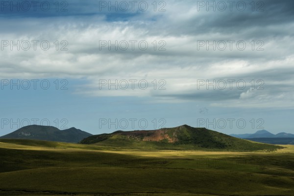 Mountains stretch across the landscape under a vast sky filled with dynamic clouds. Sancy Massif in