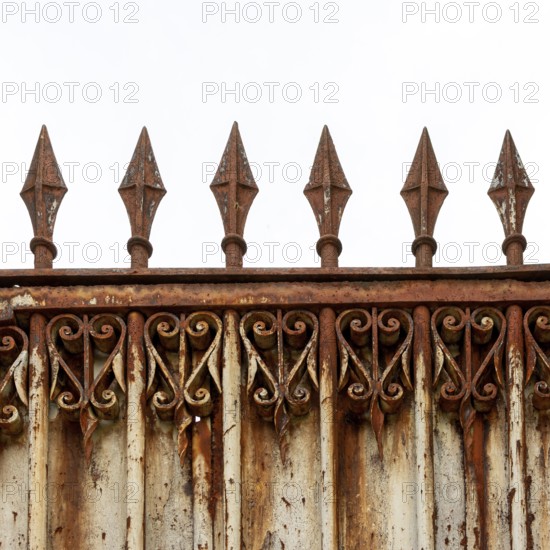 An old, weathered wrought iron fence features intricate scrollwork and pointed spikes atop its