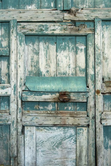 The weathered wooden door features peeling teal paint and rough textures, showcasing its rustic