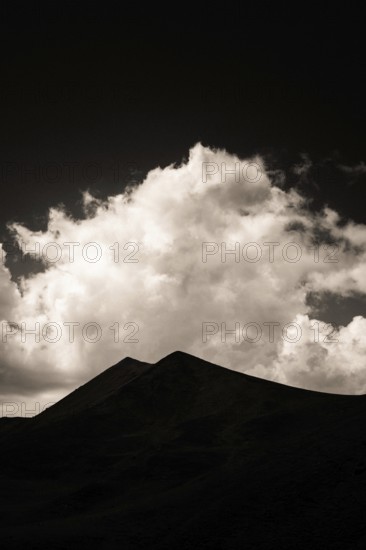 Majestic mountains form a dark outline against a backdrop of swirling clouds illuminated by