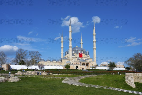 Mosque with dominant minarets and a spacious garden in front of it. Clear day with blue sky.