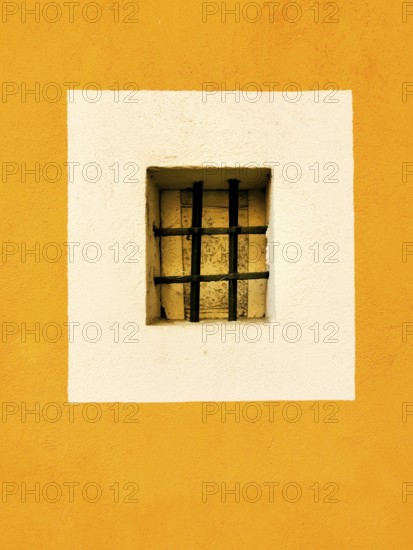 A small rectangular window with a black barred grille is centered in a white square, surrounded by