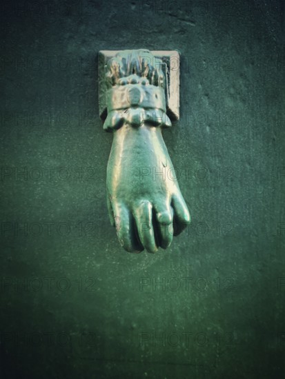 A unique green hand-shaped door knocker adorns a textured dark wall, adding a charming historical