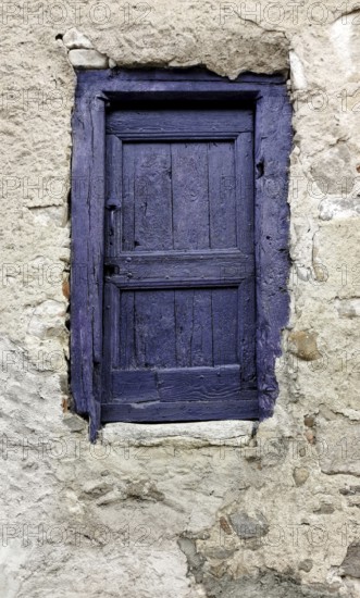 A small door painted in vibrant purple contrasts beautifully with a weathered stone wall. The