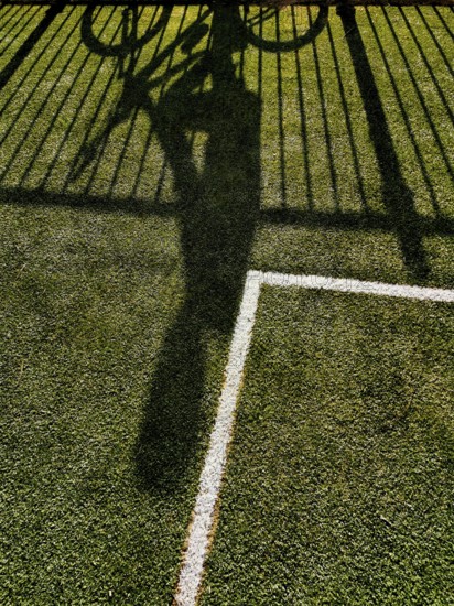 A cyclist casting a long shadow on vibrant green grass, creating a dynamic contrast with a white