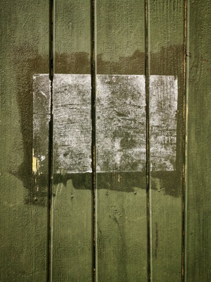 A rectangular patch on a green wooden surface shows faded remnants of a past application, with