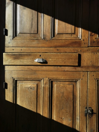 A vintage wooden cabinet features a prominent drawer, bathed in warm sunlight that casts shadows.