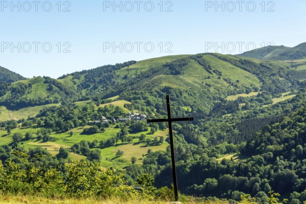 A wooden cross stands prominently against a picturesque landscape of rolling hills and vibrant