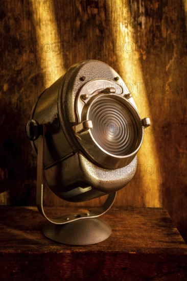 A vintage spotlight rests on a rustic wooden surface, casting a warm glow. Soft light enhances the