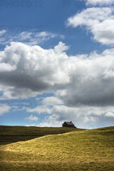 Ruined stone cottage stands alone on a grassy hillside under a partly cloudy sky in a remote
