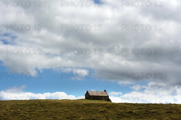A small cabin sits alone atop a grassy hill, surrounded by wide-open space. The sky is filled with