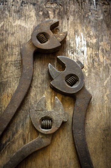 Three antique adjustable wrenches rest on a weathered wooden table, highlighting their unique