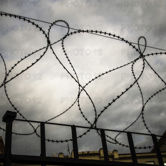 Rusty barbed wire coils twist against a dark and turbulent sky, creating a sense of confinement and