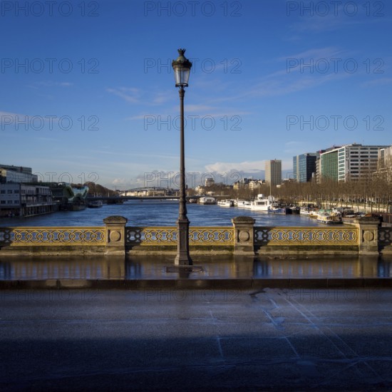 A street light stands tall on a bridge, casting light on the path as the serene Seine River flows