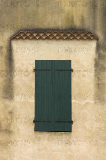 The facade features a pair of blue-green wooden shutters on a weathered wall, showcasing texture