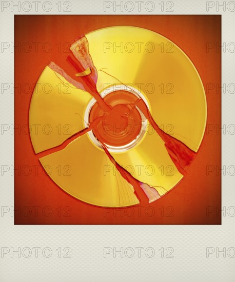 A broken polaroid compact disc lies on a bright red surface, showcasing multiple cracks radiating